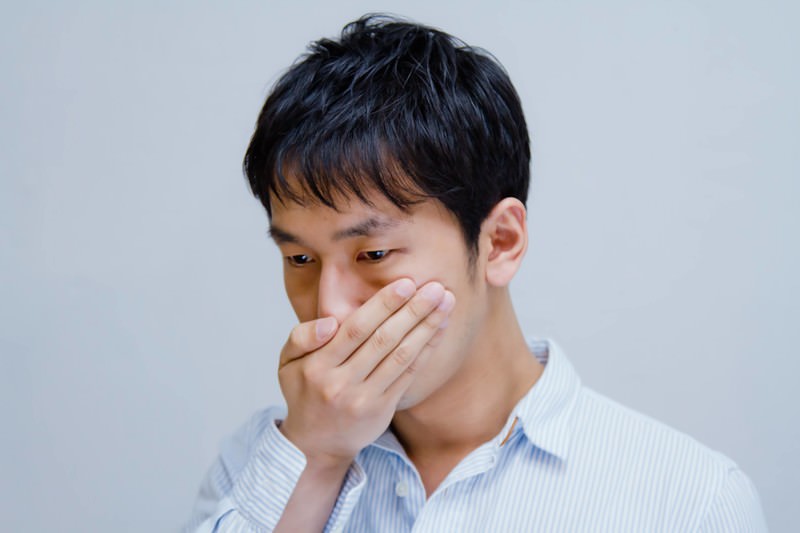 口臭が気になり口元を押さえる男性