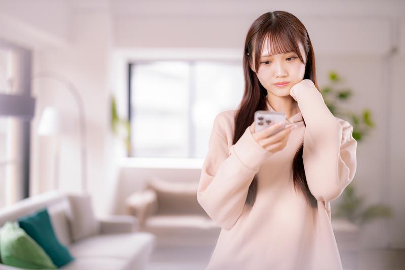 スマホでマッチングアプリを見ながら悩む女性